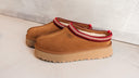 Chestnut suede UGG slippers with red patterned trim and thick soles on light background.