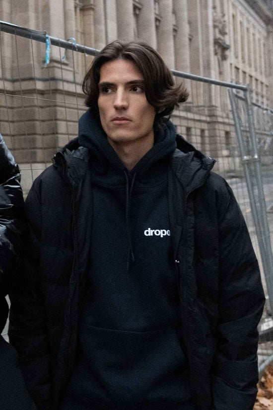 Person wearing a navy hoodie with 'dropout' logo in an urban setting