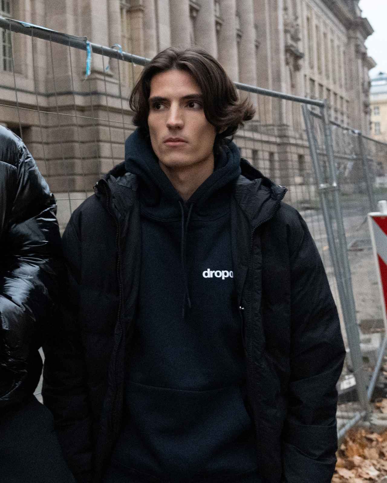 Person wearing a navy hoodie with 'dropout' logo in an urban setting