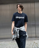 Person wearing a navy 'dropout' t-shirt and pants standing against a metallic wall.