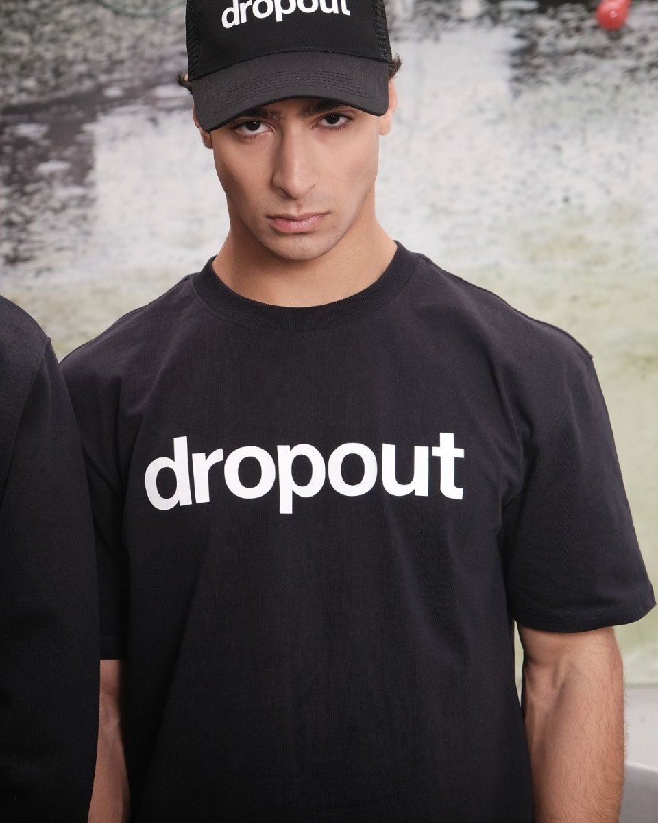 Person wearing a black 'dropout' t-shirt and cap with a blurred background