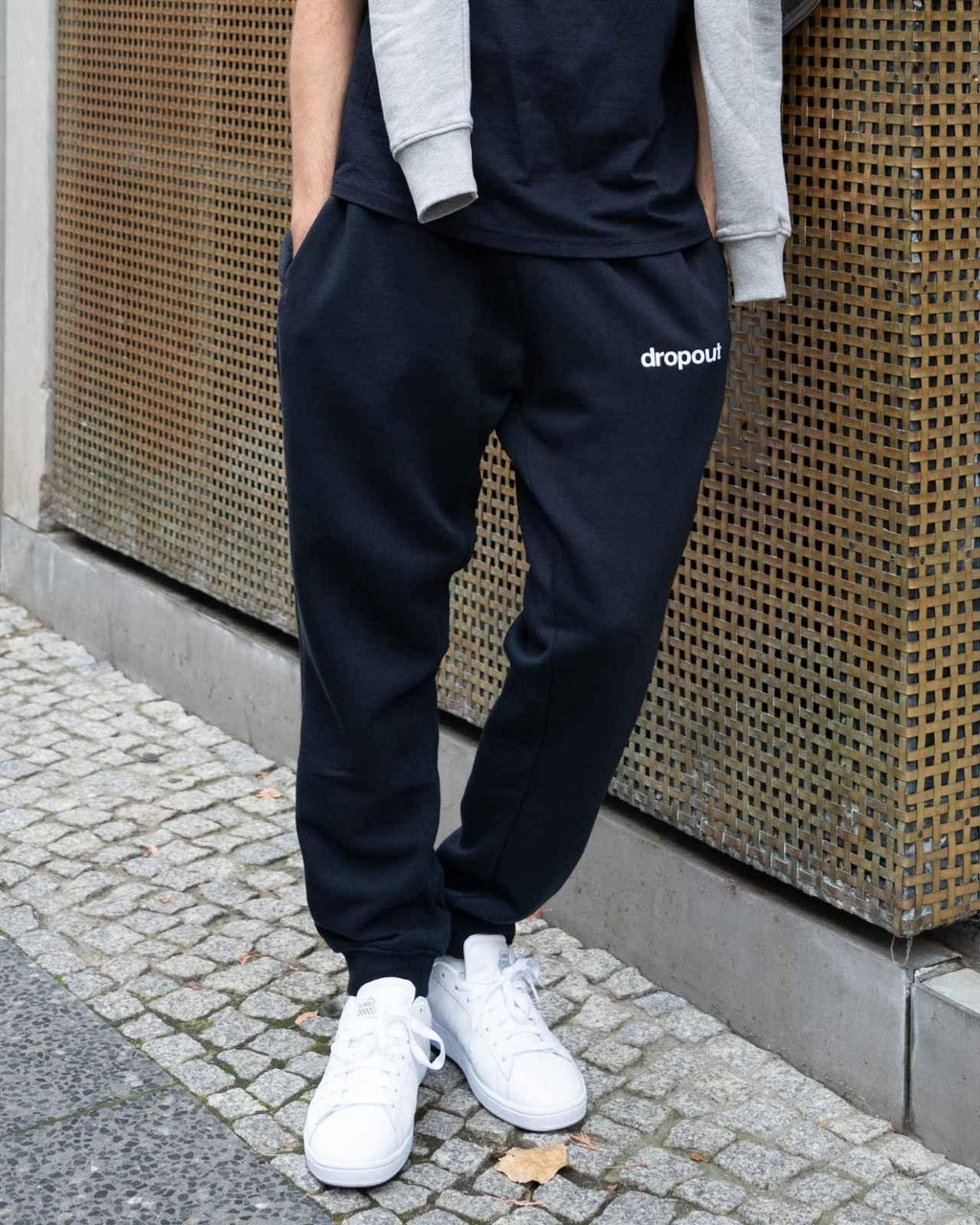 Person wearing navy 'dropout' sweatpants with a plain background