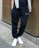 Person wearing navy 'dropout' sweatpants with a plain background