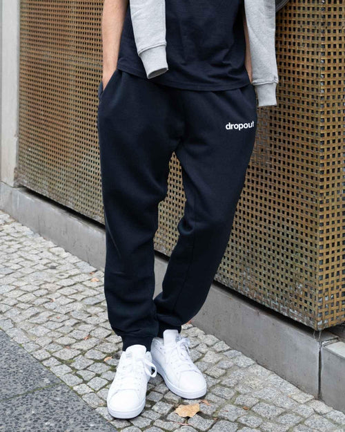 Person wearing navy 'dropout' sweatpants with a plain background