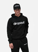 Person wearing a black 'dropout' hoodie and cap on a white background