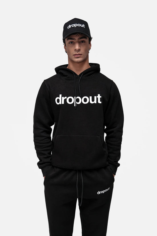 Person wearing a black 'dropout' hoodie and cap on a light gray background