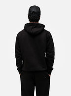 Person wearing a black hoodie and pants on a white background