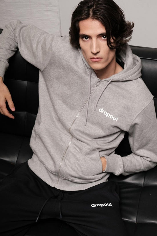 Person wearing a grey hoodie with 'dropout' logo sitting on a black leather couch.