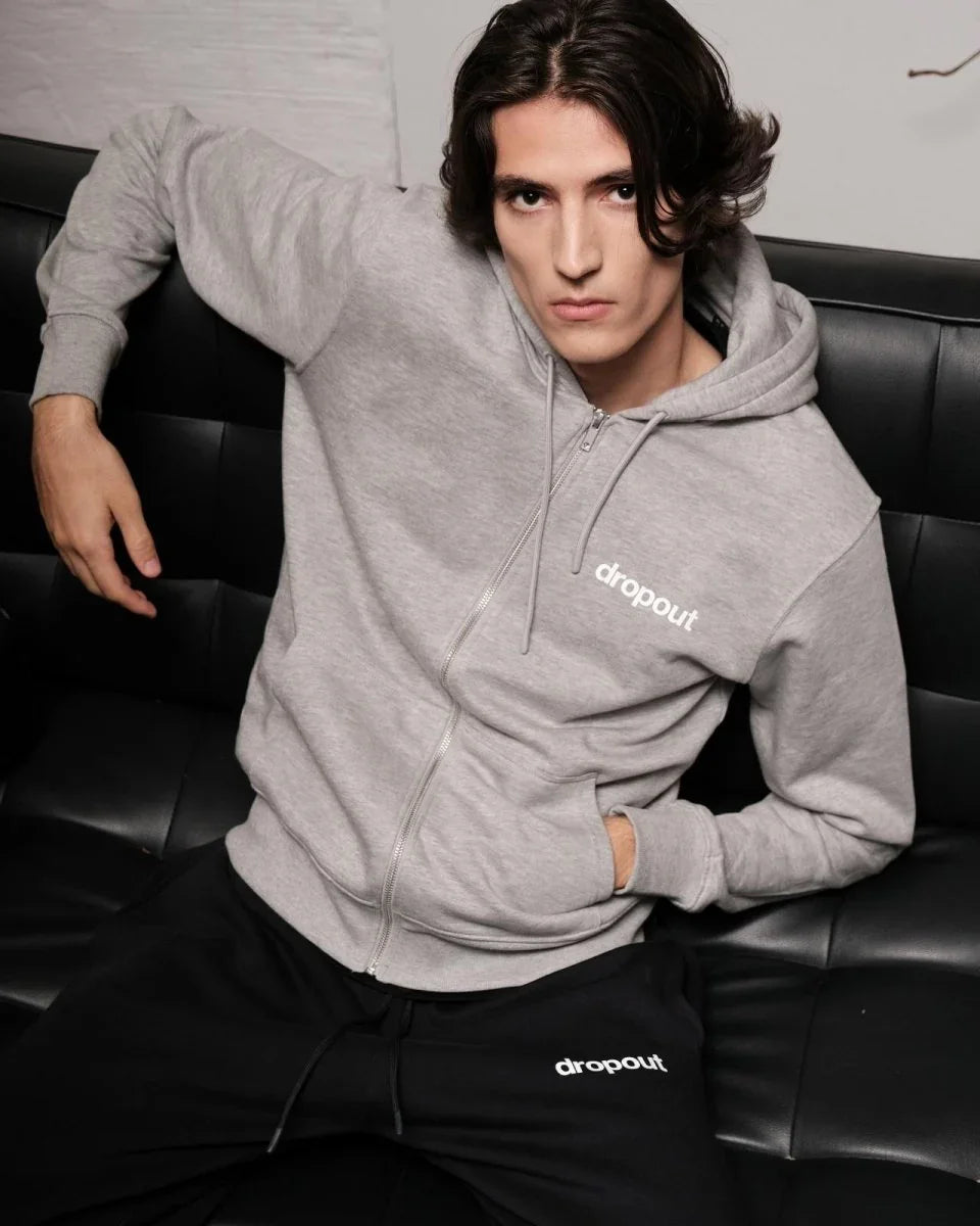 Person wearing a grey hoodie with 'dropout' logo sitting on a black leather couch.