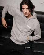 Person wearing a grey hoodie with 'dropout' logo sitting on a black leather couch.