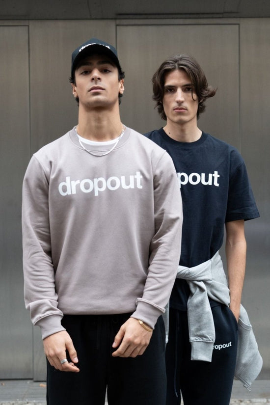 A person wearing a taupe 'dropout' branded sweatshirt standing against a neutral background