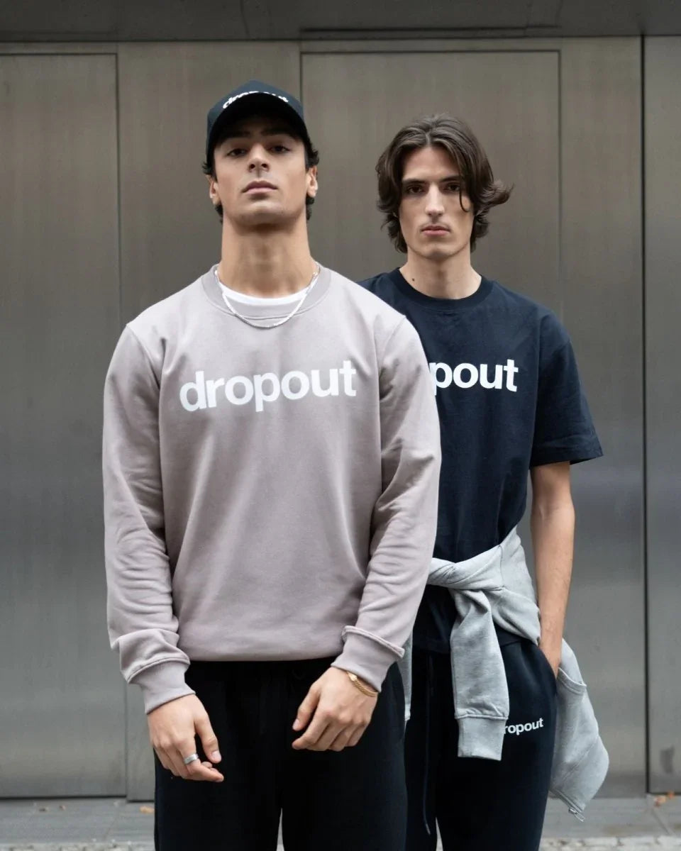 A person wearing a taupe 'dropout' branded sweatshirt standing against a neutral background