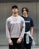 A person wearing a taupe 'dropout' branded sweatshirt standing against a neutral background