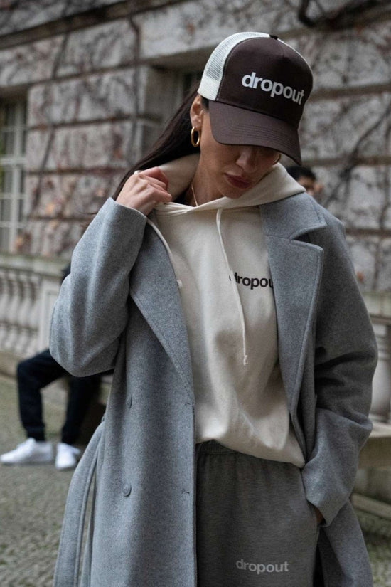 Person wearing a Beige hoodie, jacket, and Brown/Beige cap with 'dropout' branding in an urban setting.