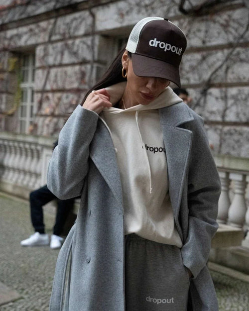 Person wearing a Beige hoodie, jacket, and Brown/Beige cap with 'dropout' branding in an urban setting.