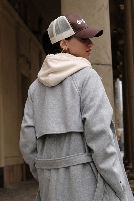 Person wearing a gray coat and a Brown/Beige cap with 'dropout' logo, standing outdoors.