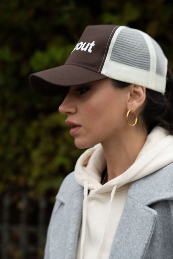 Woman wearing a Brown/Beige cap with 'dropout' text, gray coat, and beige hoodie.