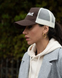 Woman wearing a Brown/Beige cap with 'dropout' text, gray coat, and beige hoodie.