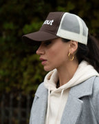 Woman wearing a Brown/Beige cap with 'dropout' text, gray coat, and beige hoodie.