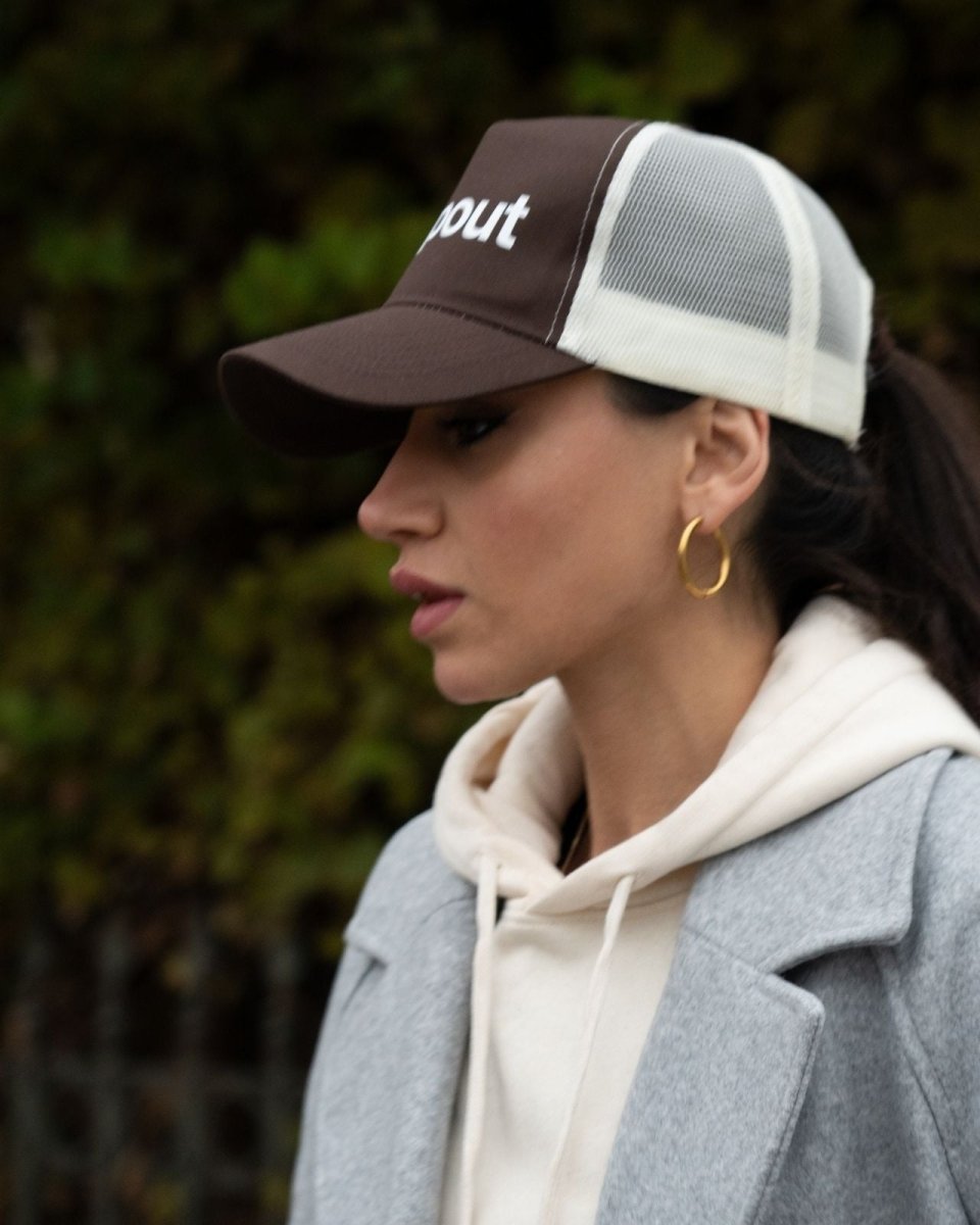 Woman wearing a Brown/Beige cap with 'dropout' text, gray coat, and beige hoodie.