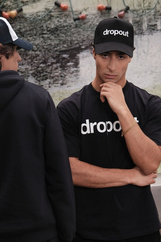 A person wearing black 'dropout' branded clothing against a textured wall.