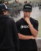 A person wearing black 'dropout' branded clothing against a textured wall.