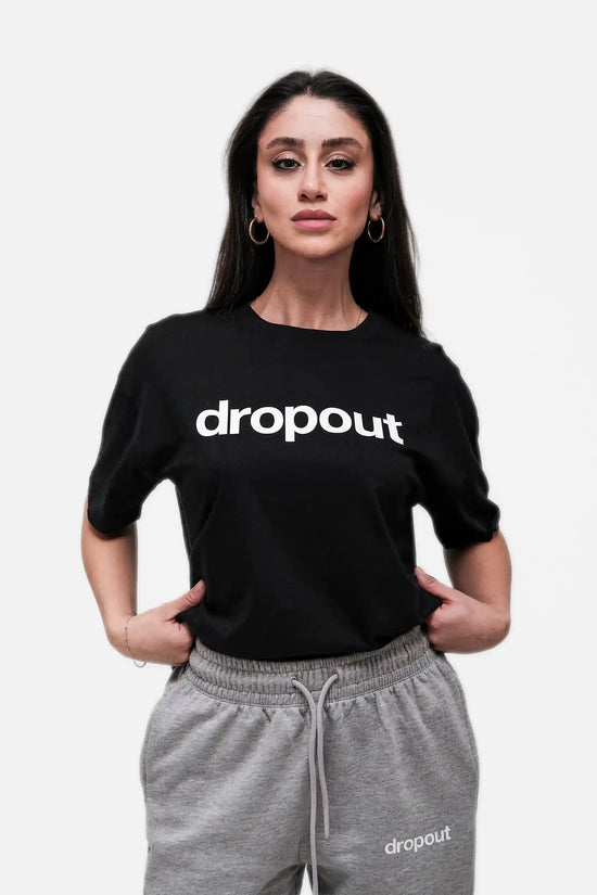 Woman wearing a black 'dropout' t-shirt and gray pants on a white background