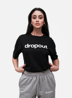 Woman wearing a black 'dropout' t-shirt and gray pants on a white background