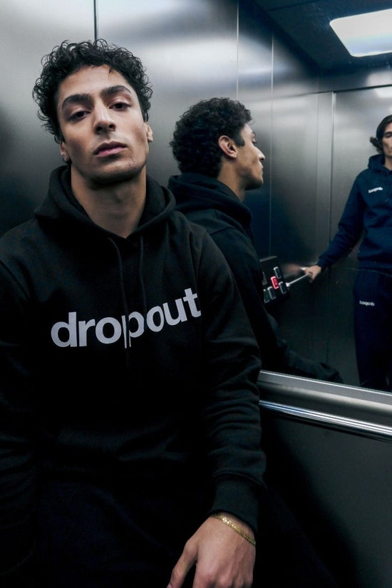 Person wearing a black hoodie with 'dropout' logo in an elevator