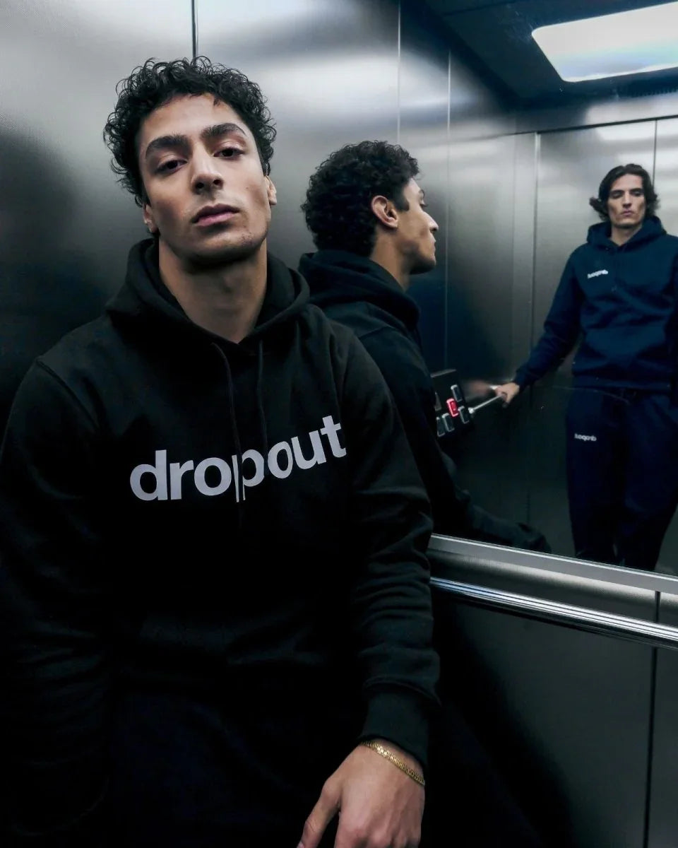 Person wearing a black hoodie with 'dropout' logo in an elevator