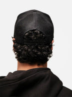 Back view of a person wearing a black mesh trucker hat and black hoodie, dropout streetwear