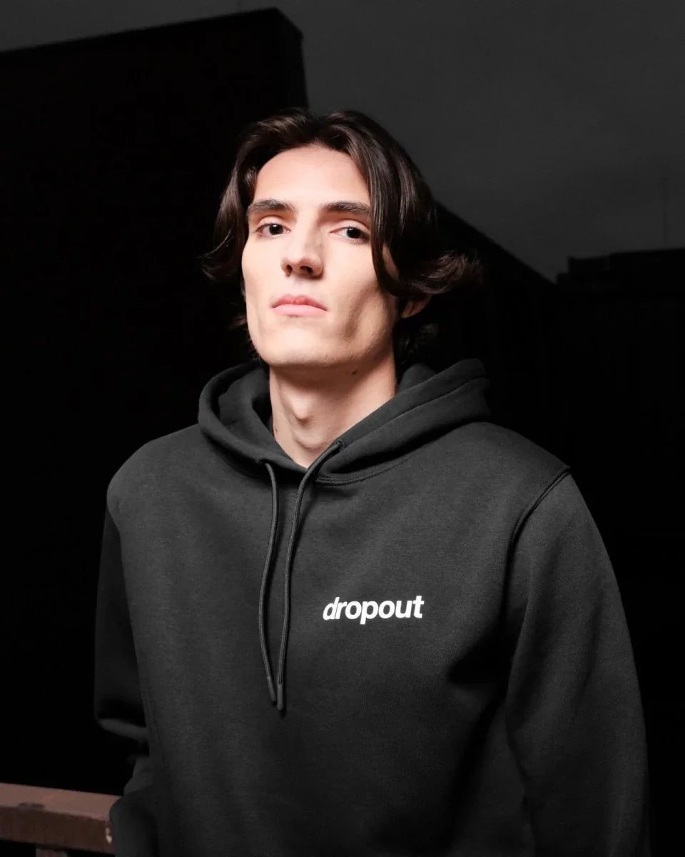 Person wearing a black hoodie with 'dropout' logo against a dark background