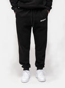 Person wearing black sweatpants with 'dropout' logo and white sneakers on a white background