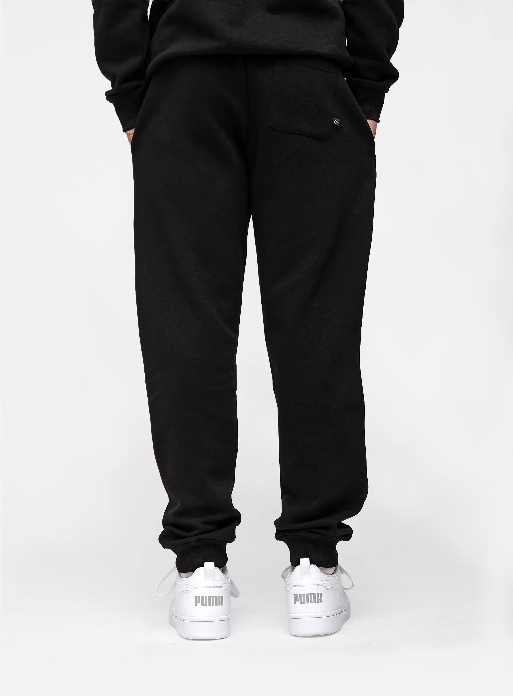 Person wearing black sweatpants and white sneakers on a white background
