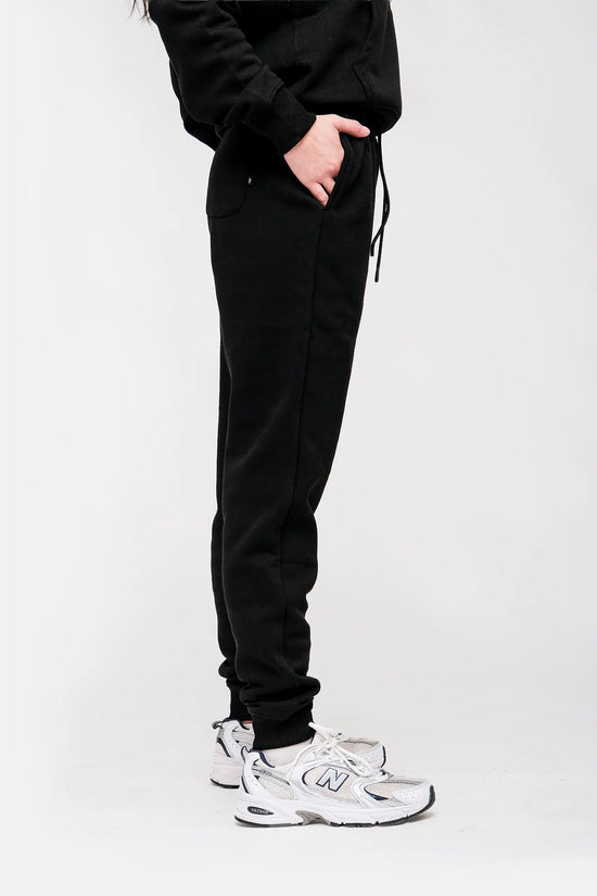 Person wearing black sweatpants and white sneakers on a white background