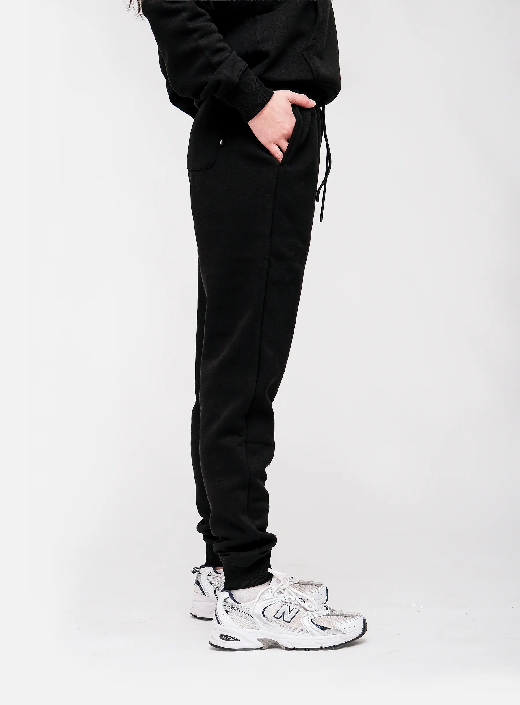 Person wearing black sweatpants and white sneakers on a white background