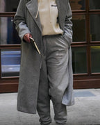 Person wearing a grey coat and matching grey sweatpants with 'dropout' branding, holding a book.