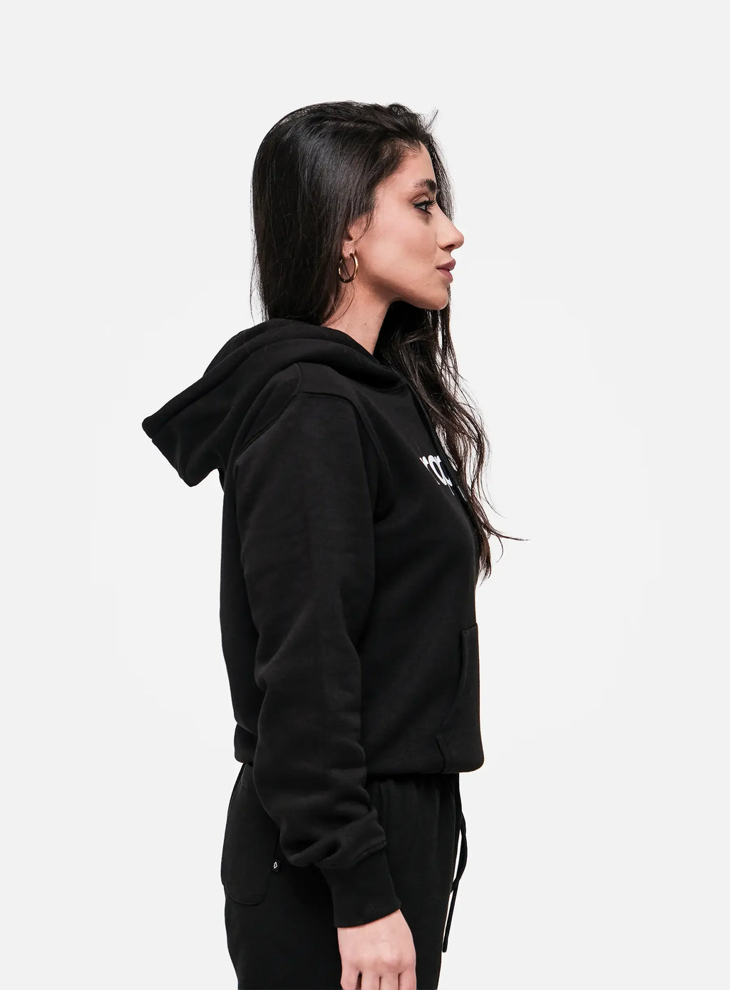 Woman wearing black streetwear hoodie and sweatpants in side profile on white background