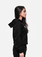 Woman wearing black streetwear hoodie and sweatpants in side profile on white background