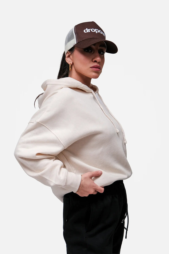 Person wearing a Beige hoodie and brown cap with 'drops' logo on a white background