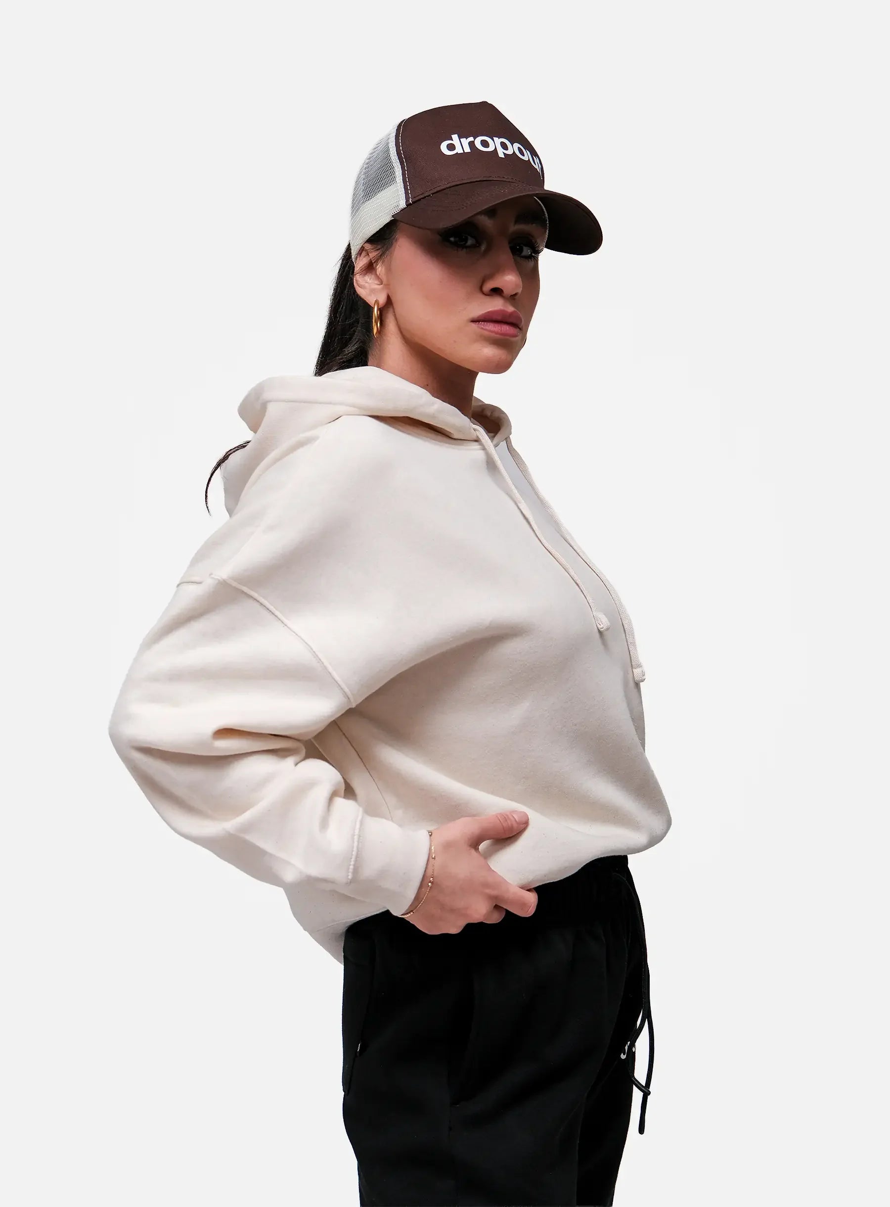 Person wearing a Beige hoodie and brown cap with 'drops' logo on a white background