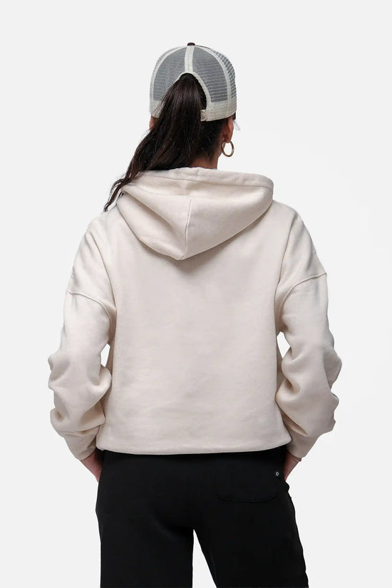 Person wearing a beige hoodie and black pants with a white and gray cap on a white background