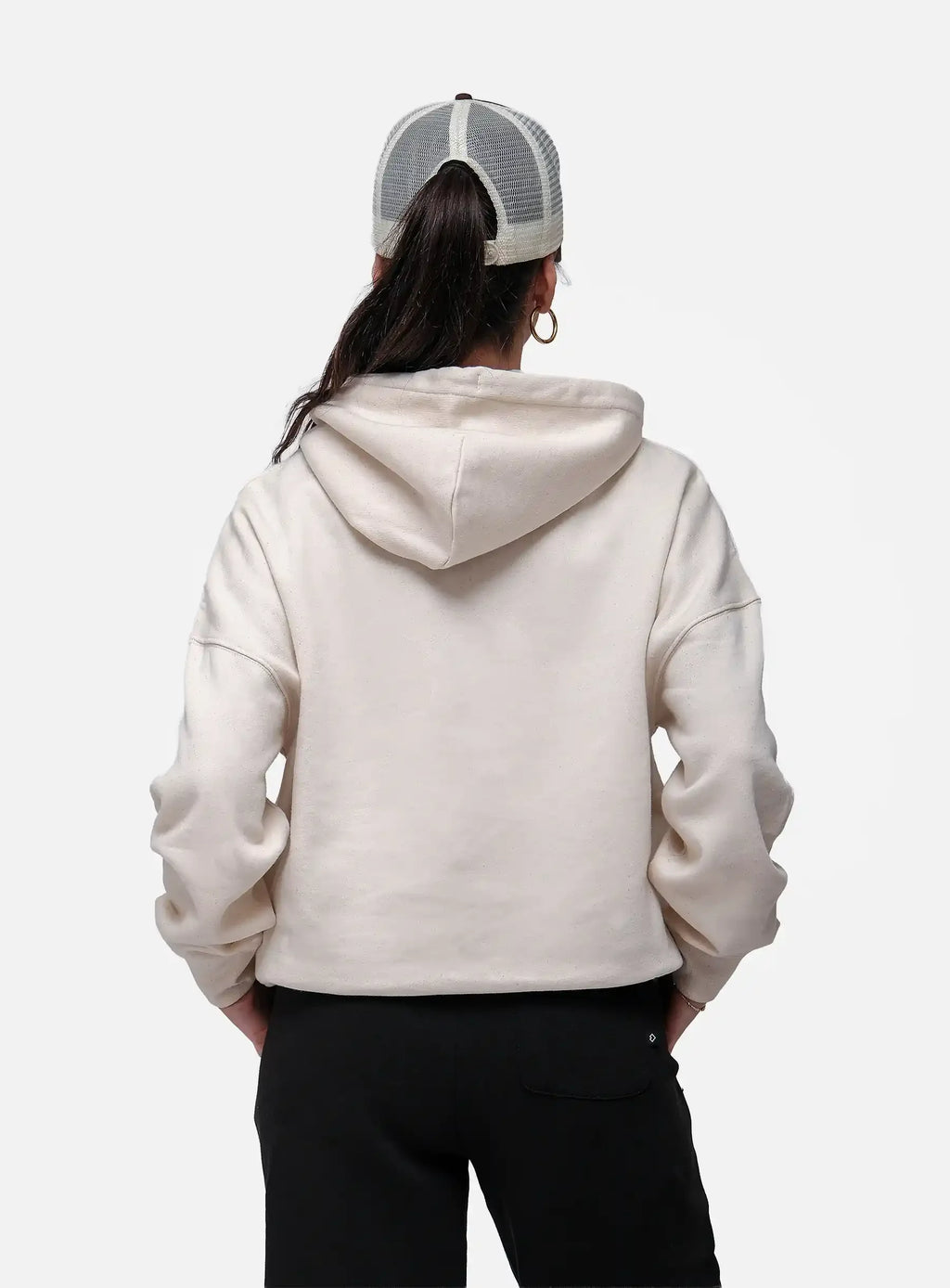 Person wearing a beige hoodie and black pants with a white and gray cap on a white background