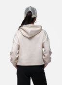 Person wearing a beige hoodie and black pants with a white and gray cap on a white background