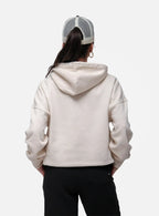 Person wearing a beige hoodie and black pants with a white and gray cap on a white background
