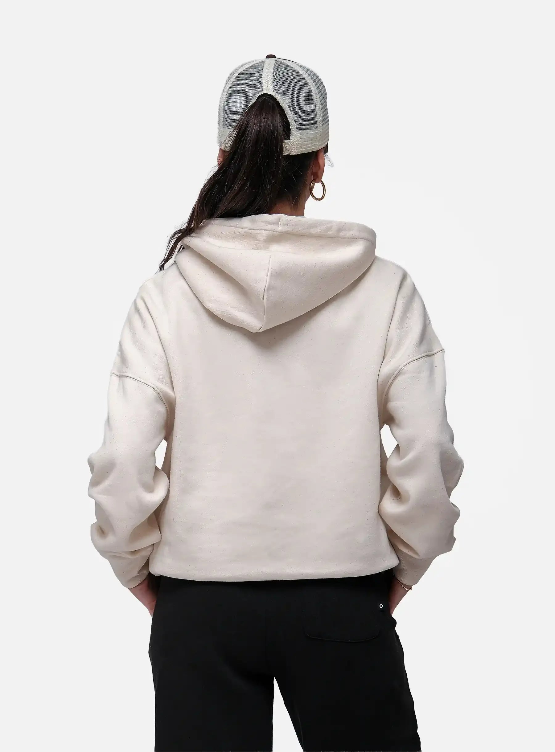 Person wearing a beige hoodie and black pants with a white and gray cap on a white background