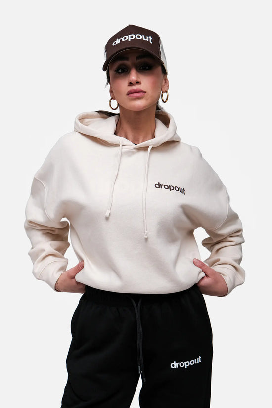 Person wearing a Beige hoodie and black pants with 'dropout' branding on a white background