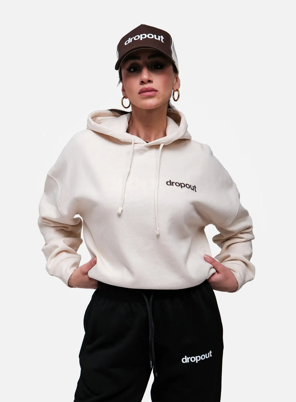 Person wearing a Beige hoodie and black pants with 'dropout' branding on a white background