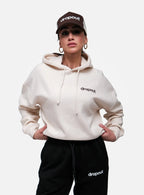 Person wearing a Beige hoodie and black pants with 'dropout' branding on a white background