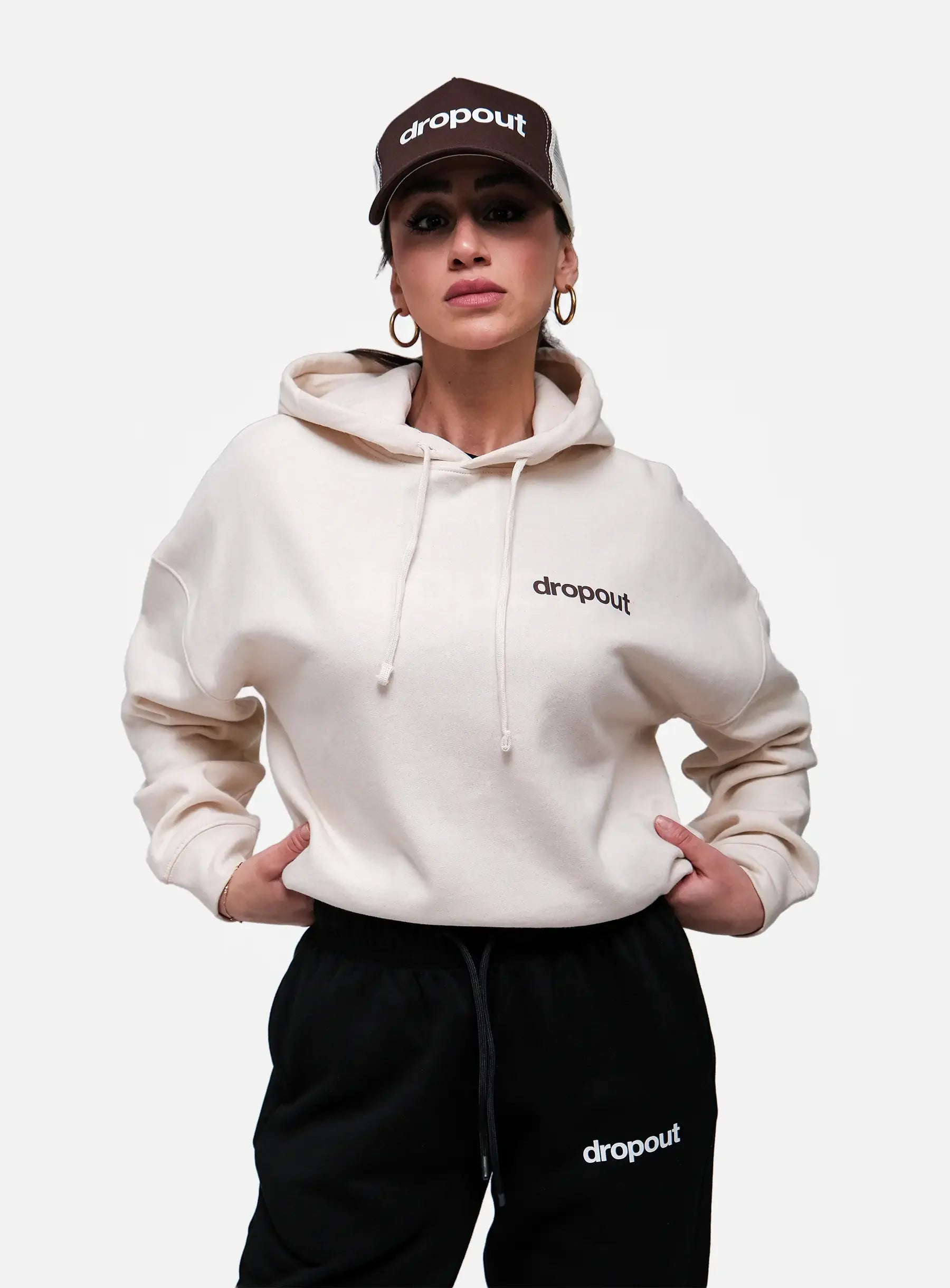 Person wearing a Beige hoodie and black pants with 'dropout' branding on a white background